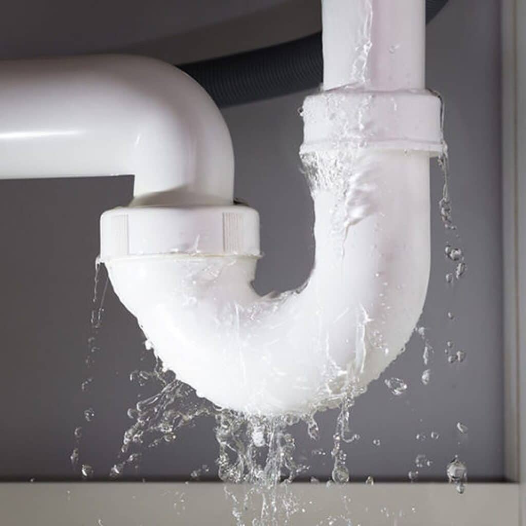 Water leaking from a white PVC pipe under a sink