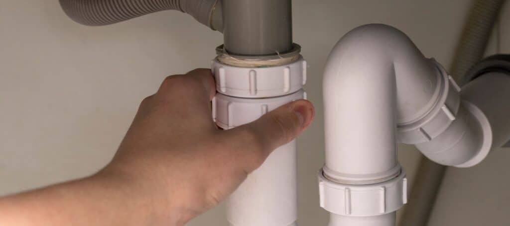 Hand tightening a plastic pipe connection under a sink to prevent leaks