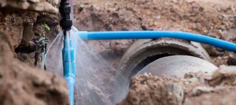 Close-up of a broken blue water pipe spraying water during an underground leak