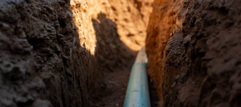 A blue water pipe installed in a freshly dug trench through packed soil