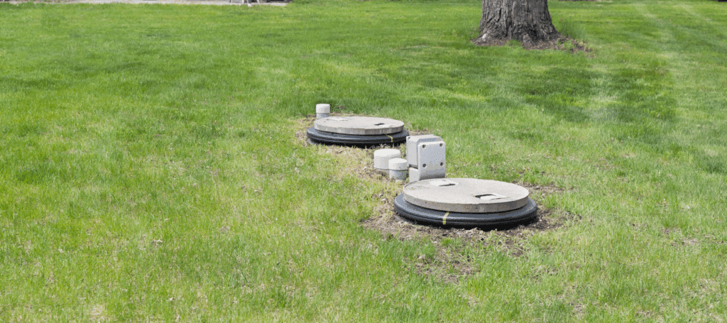 Two circular septic tank covers and ventilation pipes visible in a grassy residential yard