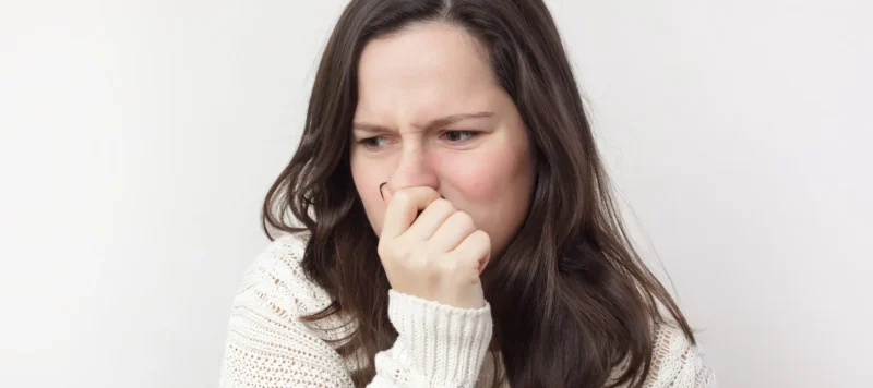 woman with long brown hair and a white sweater pinching her nose due to bad smell.